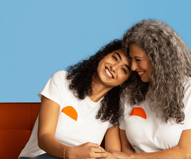 Mother and daughter smiling and hugging on an orange couch against a blue wall